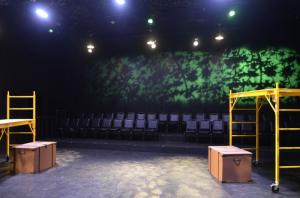 An empty theater stage with yellow scaffolds, brown boxes, and a green light pattern in the background.