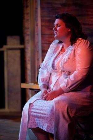 A woman sitting down on a prop porch under moody lighting in a long white dress
