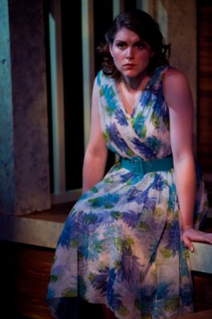 A woman seated on the edge of a stair wearing a floral dress in moody lighting