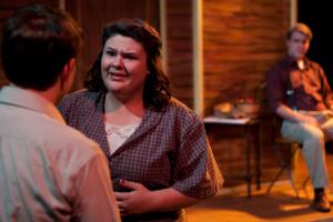 A woman talking to a man looking very concerned in front of a prop house on a porch for a theatre performance