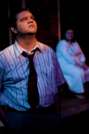 A man stood in shirt and tie looking up at the ceiling with a spotlight on his face