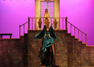 Two people on a theatrical stage with a purple-lit stone staircase.