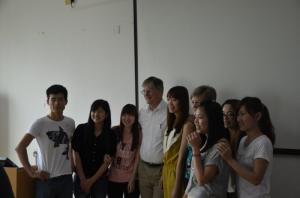 A group of nine people posing together in a room with a white wall and screen.