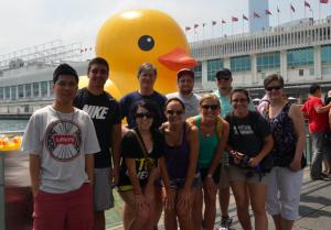 a group photo of people standing outside in front of a large rubber duck inflatable