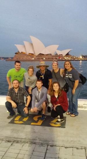 Group posing in front of the Sydney Opera House at dusk.