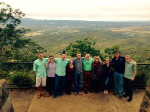 A group of nine people posing on a viewing platform overlooking a vast landscape of hills and valleys.