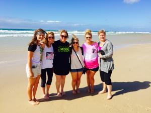 A group of six people standing on a beach with waves in the background.