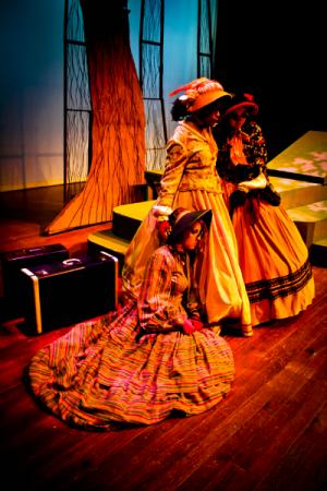 2 women standing in bright yellow clothing with a suitcase on the floor beside them, bright lighting showcasing the people