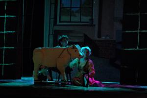 A woman and a man sitting on the floor beside a prop of a cow in old clothing and dim lighting