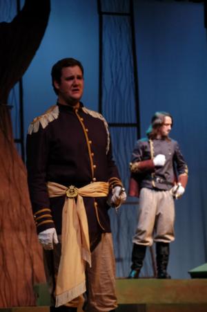 2 men standing on a stage in old military style clothing with a dim background