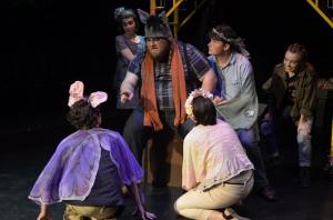 Actors in costume perform a theatrical scene on a dark stage.
