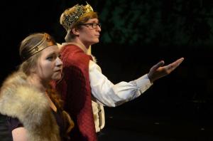 Two actors in royal costumes, one with a crown and fur, the other with a crown and cape, on stage.