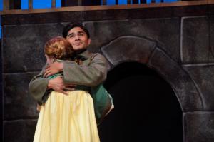 Two people on stage embracing in front of a stone-like archway backdrop.