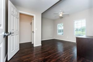 Empty room with dark wood floors, two windows, and a ceiling fan.