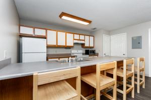 A modern kitchen with a gray countertop, wooden stools, and white appliances.