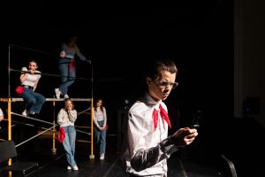 The man is in the foreground looking at a phone in front of four women in Working: The Musical Theatre production.