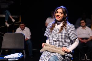 A woman sits in the foreground, and a small group of men sits in the back in Working: The Musical Theatre production.