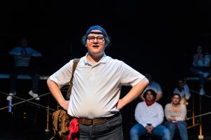 The man is in the foreground posing in front of sitting actors in Working: The Musical Theatre production.