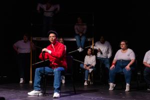 Men in the foreground sitting in front of a group of actors in Working: The Musical theatre production.