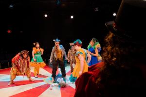 Woman stands over woman on ground while others circle around during Cagebirds Theatre Production 