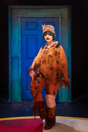 Woman standing on one leg in front of blue door during Cagebirds Theatre Production