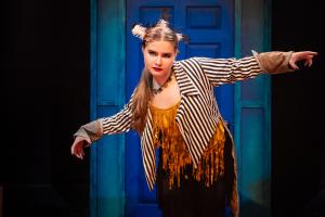 A woman posing in front of a blue door during Cagebirds Theatre Production.