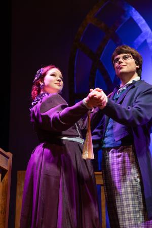 Two people in period costumes holding hands, performing on stage.