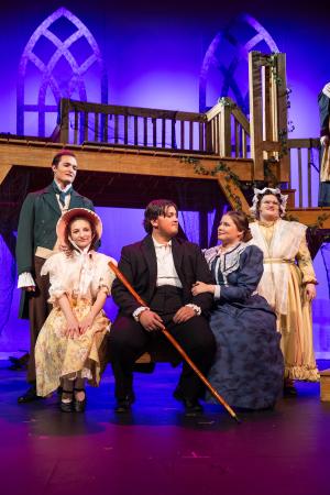 Group of five people in period costumes on a stage with a wooden balcony and arched windows in the background.