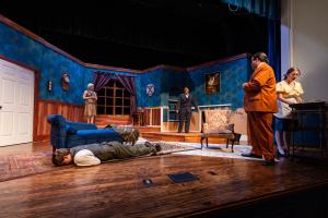 Stage play set in a living room with actors performing.