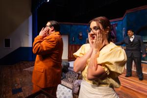 Three actors on stage, two in the foreground with surprised expressions.