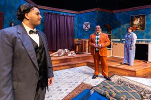 Actors on stage in a dramatic room setting with blue walls and elegant furnishings.