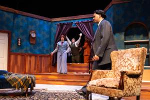 A scene from a stage play depicting a vintage living room with characters in period costumes.