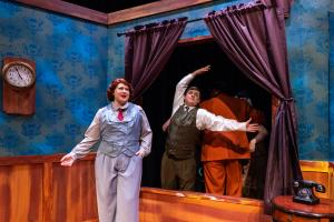 Actors perform on a stage set resembling a vintage room with blue wallpaper and wooden accents.