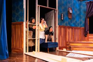 Three people look through a doorframe on a theater stage with a vintage room set.