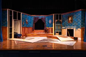 A stage set resembling a room with blue wallpaper, a central doorway, and scattered construction pieces.