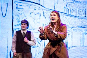 One male and female ETBU Theatre student acting on stage with a bright screen behind them.