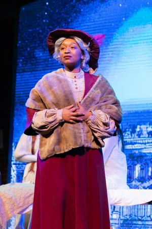 A woman stood on a stagr in a long red dress and fur coat