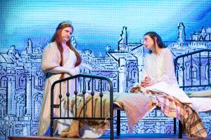 2 people talking on a stage on a bed with a line drawn background
