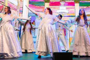 People dancing together in white clothing on a brightly lit stage