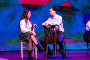 2 people sat on chairs talking to eachother on a stage during a play