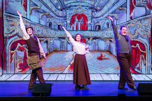 3 people with arms up in formal clothing on a stage