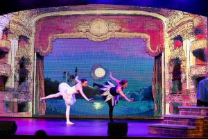 Two ballet dancers, one in white and one in black, perform on stage against a backdrop of an ornate theater and a moonlit lake, conveying grace and drama.