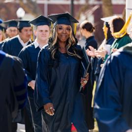 Students walking down a sidewalk in navy academic regalia.