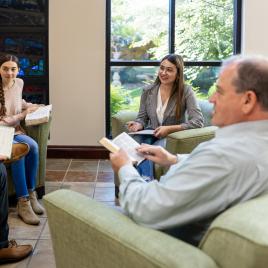 A group of people sitting inside reading books in front of a window