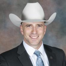 a man in a suit and white cowboy hat against a gray backdrop