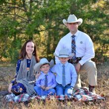 Family of four sitting on a blanket outdoors, wearing cowboy hats and casual attire.