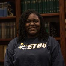 A woman smiling at the camera in front of bookshelves.