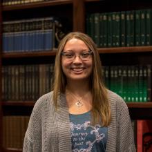 A woman smiling at the camera in front of bookshelves.