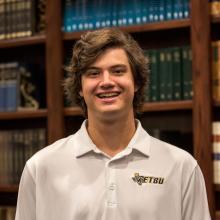 A man smiling at the camera in front of bookshelves.