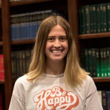 A woman smiling at the camera in front of bookshelves.